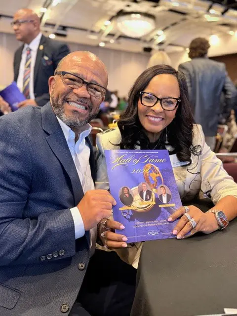 Two smiling people holding a magazine with a purple cover.