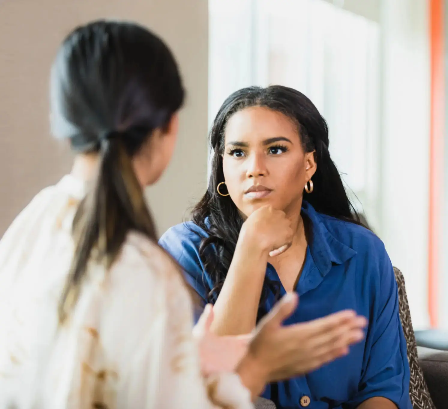 Two women engaged in a serious conversation indoors.