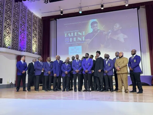 Group of men in suits standing on stage under a projection screen.