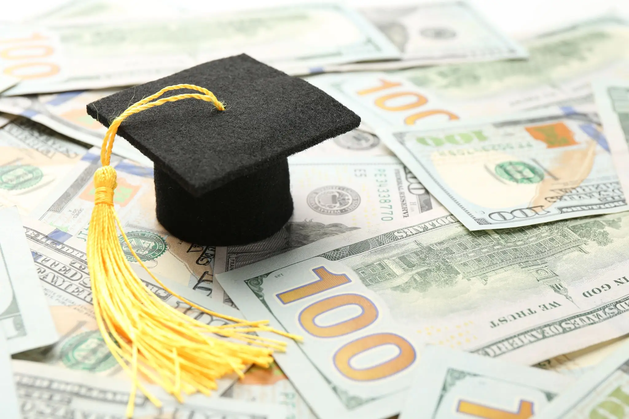 Graduation cap on hundred-dollar bills symbolizing education cost.